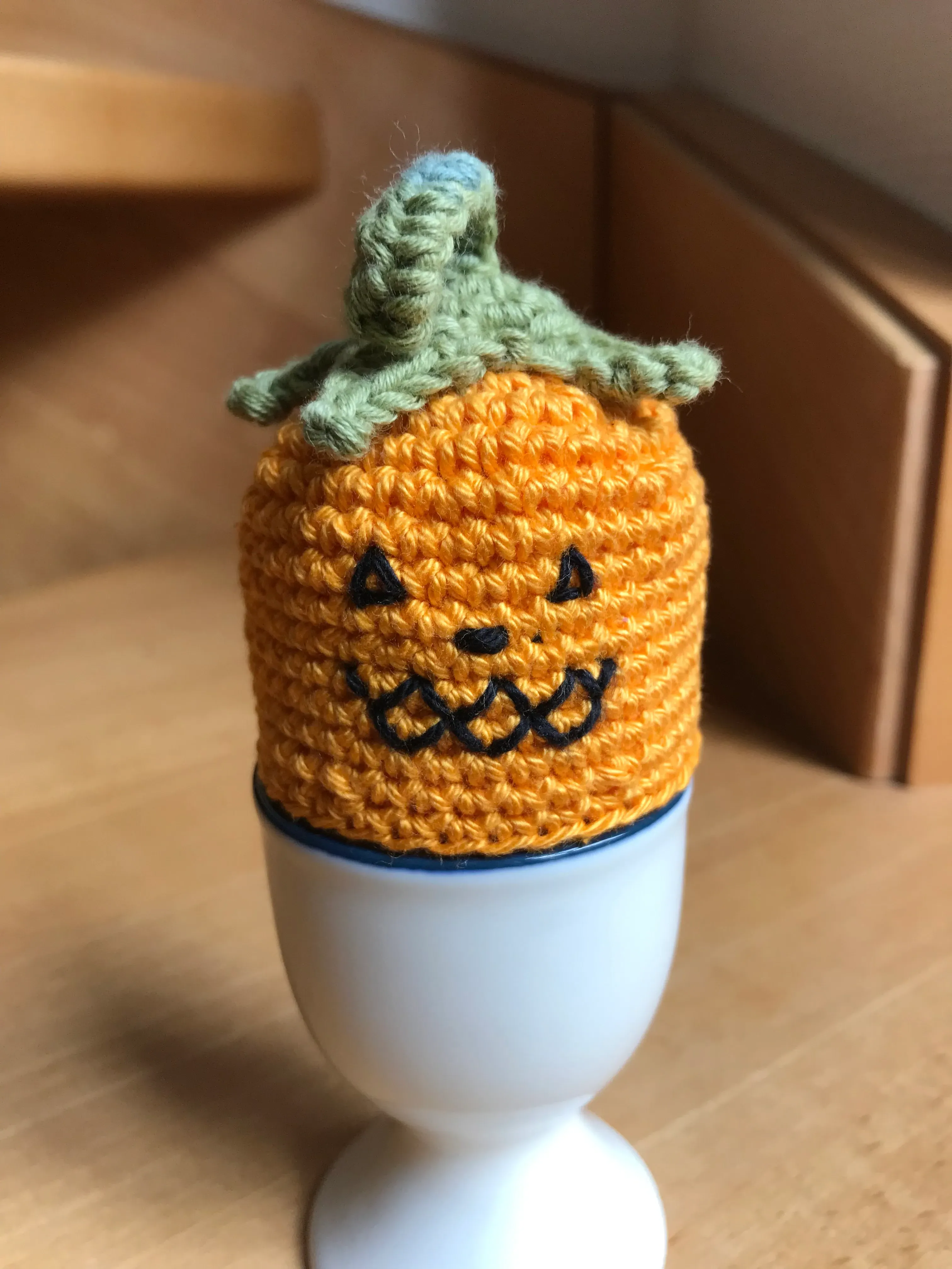 Eierwärmer Kürbis aufgesticktes Gruselgesicht, grüner Blattansatz